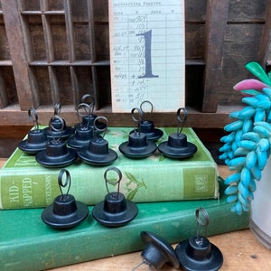 May include: Nine black metal bookends with a spring wire on top. The bookends are sitting on top of two green books. The bookends are used to hold open books or papers.