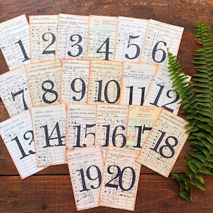 May include: A collection of twenty vintage library checkout cards arranged in a grid, each featuring a large black printed number from 1 to 20. The off-white paper cards contain handwritten text, stamped dates, and columns for tracking book loans.