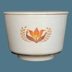 Könnte beinhalten: Cremefarbener Keramikbehälter mit Deckel, verziert mit einem orangefarbenen, braunen und gelben Blumendesign und Blattmuster. Der Behälter hat eine ausgestellte Form und einen dekorativen Sockel. Vintage-Küchenartikel.