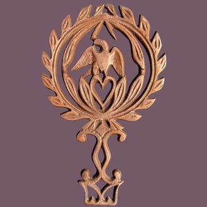 May include: A bronze-colored decorative metal piece featuring an eagle within a laurel wreath. Below the eagle is a heart-shaped design. The piece has an ornate, symmetrical design with a decorative base.