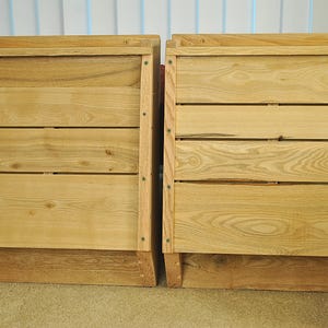 May include: Two wooden storage boxes with a natural finish. Each box is constructed with horizontal wooden slats and a solid frame. The boxes are designed with a slightly angled base and are suitable for various storage needs.