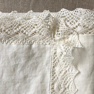 May include: A white linen tablecloth with a delicate white crocheted lace trim. The lace trim is intricate and has a scalloped edge.
