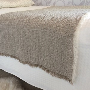 Könnte beinhalten: Eine braune Leinen-Decke mit einer strukturierten Webart und Fransen an den Rändern. Die Decke liegt auf einem weißen Bett.