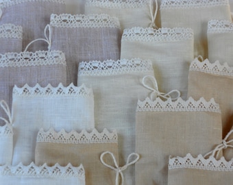 May include: A collection of small, white fabric bags with lace trim. The bags are arranged in a pile, with some of the bags overlapping.