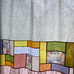 Puede incluir: Una cortina de lino blanco con un diseño de patchwork en tonos de amarillo, naranja, verde, rosa y morado. La parte inferior de la cortina tiene un ribete rosa con volantes.