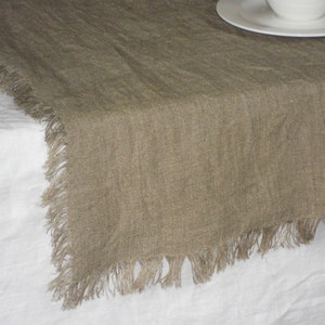 Peut inclure: Un chemin de table en lin brun avec des bords effilochés. Le chemin de table est posé sur une nappe en lin blanc.