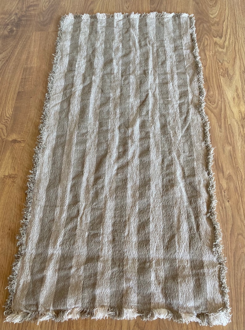 Puede incluir: Un camino de mesa de lino a rayas beige y blanco con bordes deshilachados.