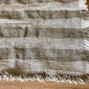 Puede incluir: Primer plano de una tela rayada beige y marr&oacute;n con un borde deshilachado. La tela tiene una textura natural de lino.