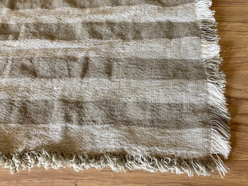 Puede incluir: Primer plano de una tela rayada beige y marr&oacute;n con un borde deshilachado. La tela tiene una textura natural de lino.