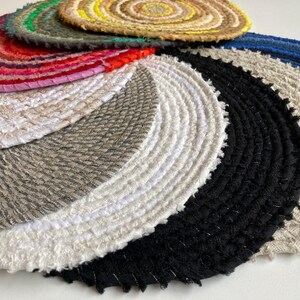 Könnte beinhalten: Ein Set runder, gewebter Tischsets in verschiedenen Farben und Texturen, darunter Weiß, Schwarz, Grau und Beige. Die Tischsets sind kreisförmig angeordnet, wobei das größte Tischset in der Mitte und das kleinste Tischset außen liegt.