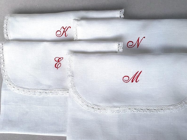 May include: White linen pouches with scalloped lace trim and embroidered red initials. The pouches are in various sizes and feature the letters K, E, N, and M. These pouches are ideal for storing small items.