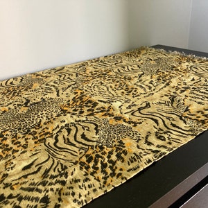 Puede incluir: Un camino de mesa beige con un diseño de estampado animal negro y naranja. El estampado presenta una combinación de patrones de leopardo y cebra.