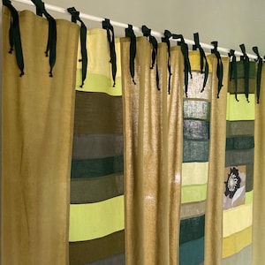 Puede incluir: Cortina decorativa con diseño de patchwork. Presenta varios tonos de verde y amarillo, con un acento floral. Cuelga de una barra blanca con lazos negros. La estética general es natural y terrosa.