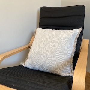 May include: A wooden chair with a black cushion and a white patterned pillow. The chair has a light wood frame and a curved back.
