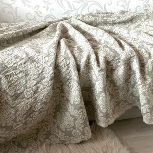 May include: A soft, beige throw blanket with a white damask pattern. The blanket is folded and draped over a couch.