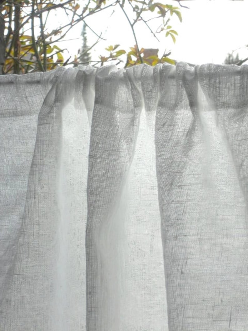 May include: White sheer curtains with a gathered top, hanging in a window. The curtains are made of a lightweight fabric with a subtle texture.
