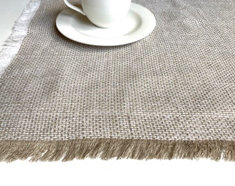 Puede incluir: Un mantel individual beige con borde de flecos. El mantel individual está hecho de un tejido tejido con una textura sutil.