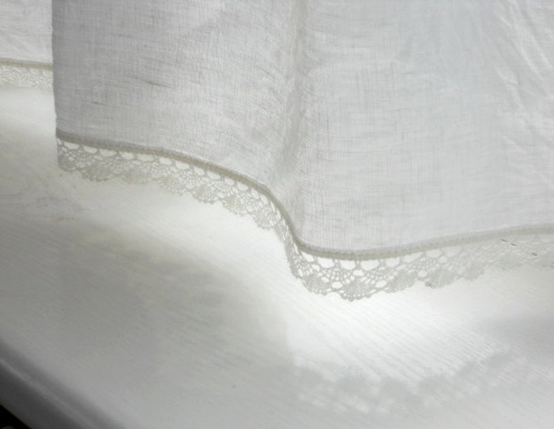 May include: White sheer curtain with a delicate lace trim. The curtain is hanging in a window and the lace trim is visible at the bottom.