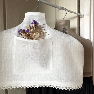 Puede incluir: Percha de ropa de lino blanco con ribete de encaje y un bolsillo para guardar objetos pequeños. Hay flores secas en el bolsillo.
