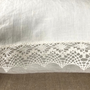 May include: White pillow with a white lace trim. The pillow is made of a soft, linen fabric.