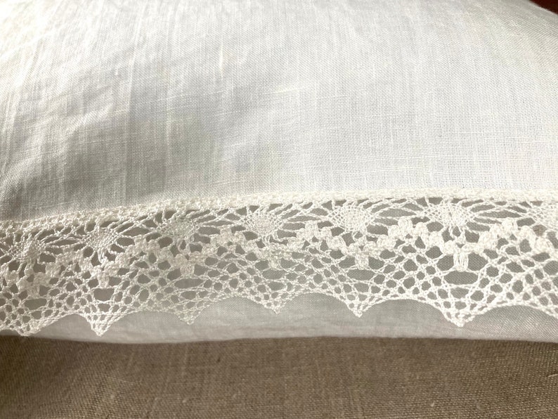 May include: White pillow with a white lace trim. The pillow is made of a soft, linen fabric.
