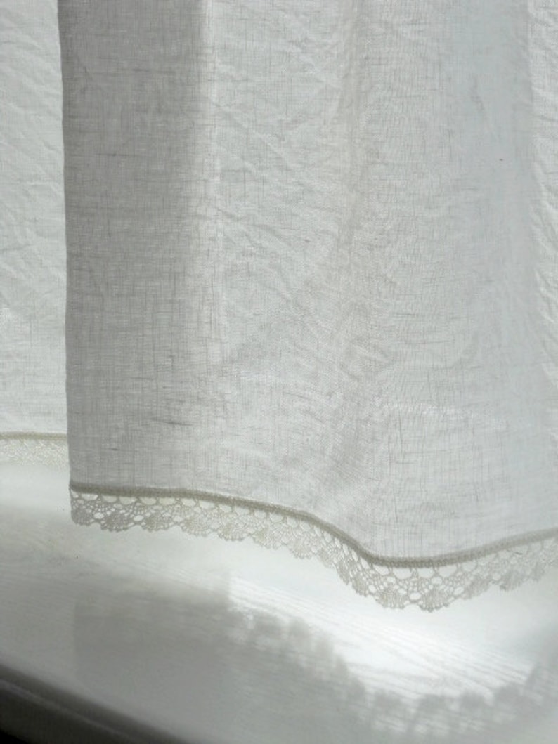 May include: White sheer curtain with a delicate lace trim. The curtain is hanging in a window and the light is shining through it.