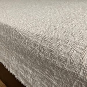 以下が含まれることがあります： 白の編み地の毛布で、質感のある模様があります。毛布はほつれた縁を持っています。