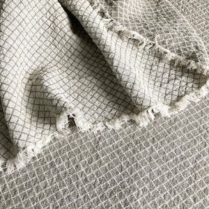 Peut inclure: Gros plan sur un tissu tissé beige et brun avec un motif en losange. Le tissu a un bord effiloché.