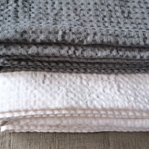 May include: A stack of two waffle weave towels, one grey and one white. The towels are folded and have a textured surface.