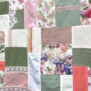 Puede incluir: Una colcha de retazos con una variedad de patrones florales en tonos de rosa, verde y blanco. La colcha está hecha de diferentes telas, incluyendo lino, algodón y encaje.
