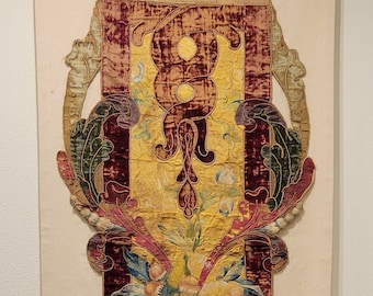 May include: A vintage tapestry featuring a gold, red and green floral design. The tapestry is framed in a wooden frame and mounted on a white wall.