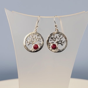 May include: Silver tree of life earrings with a red gemstone in the centre of each earring.