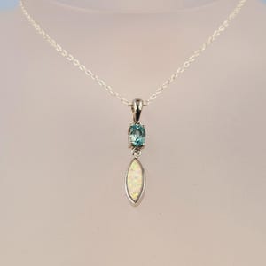 May include: A silver chain necklace with a pendant featuring a light blue oval gemstone and a teardrop-shaped white opal.