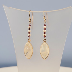 May include: Gold dangle earrings with a pearlescent white oval stone and a chain of small white and burgundy beads.