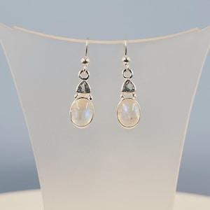 May include: Silver dangle earrings with a white moonstone oval and a smaller triangular green gemstone.