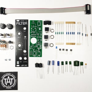 Op de afbeelding: Een kit voor het bouwen van een 12db-1p filter, met een groene printplaat met componenten, knoppen en weerstanden. De kit bevat een zwart paneel met de tekst "12db-1p FILTER" en "LEP-TAT".
