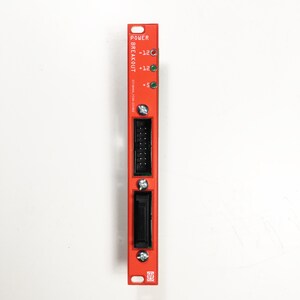 Può includere: Una scatola di derivazione di alimentazione rossa con un connettore nero e indicatori LED per -12, +12 e +5 volt. La scatola è etichettata "POWER BREAKOUT" e ha il testo "3218444-1240-210001".