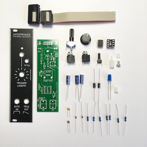 Puede incluir: Una placa de circuito verde con texto negro que dice "GATE TRIGGER /envelope generator)" y "TRIGGER LENGTH". La placa está rodeada de varios componentes electrónicos, incluyendo resistencias, condensadores, potenciómetros, interruptores y un LED azul.