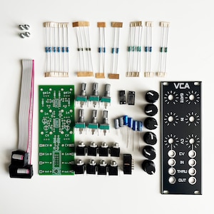 May include: A kit for building a VCA module for electronic music synthesis. The kit includes a green circuit board with potentiometers, jacks, and resistors, a black panel with knobs and labels, and various electronic components.