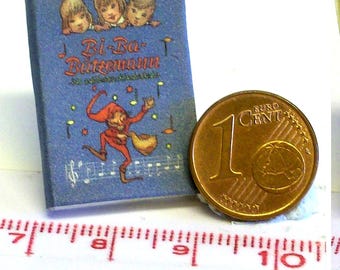 以下が含まれることがあります： 子供と道化師のイラストが描かれた「Bi-Ba-Butzemann」というタイトルのミニチュアの青い本。本の隣には1セントユーロ硬貨があります。定規は測定値を示しています。