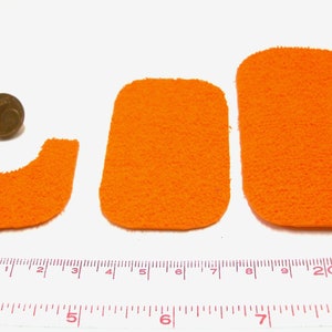 Peut inclure: Trois formes de tapis en feutre orange, dont un rectangle, un rectangle arrondi et un U. Les formes sont disposées sur une surface blanche avec une règle pour l'échelle.