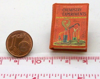 May include: Miniature orange book titled "The Golden Book of Chemistry Experiments" with illustrations of beakers and flasks. A one-cent Euro coin is next to the book. The book is approximately 1.5 inches tall.