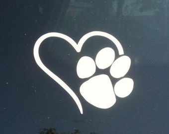 May include: White vinyl decal of a paw print inside a heart shape. The decal is on a dark blue car window.
