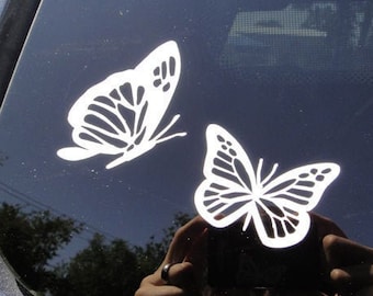 May include: Two white butterfly decals on a dark gray car window.