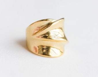 May include: A gold-toned ring with a unique, abstract design. The ring is made of a smooth, shiny metal and has a slightly curved shape.