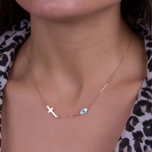 Puede incluir: Un collar de oro rosa con un pequeño dije de cruz y un dije de ojo azul.