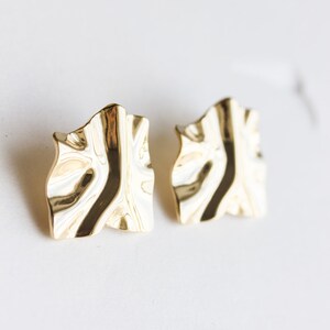 May include: A pair of gold-tone earrings with a textured, wavy design. The earrings are a modern and stylish accessory.