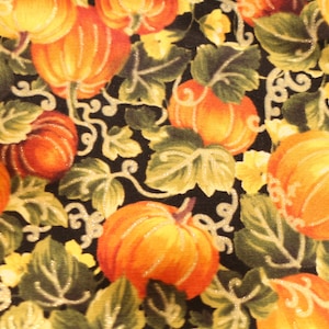 May include: A black fabric with a repeating pattern of orange and yellow pumpkins with green leaves. The pumpkins are various sizes and shapes.