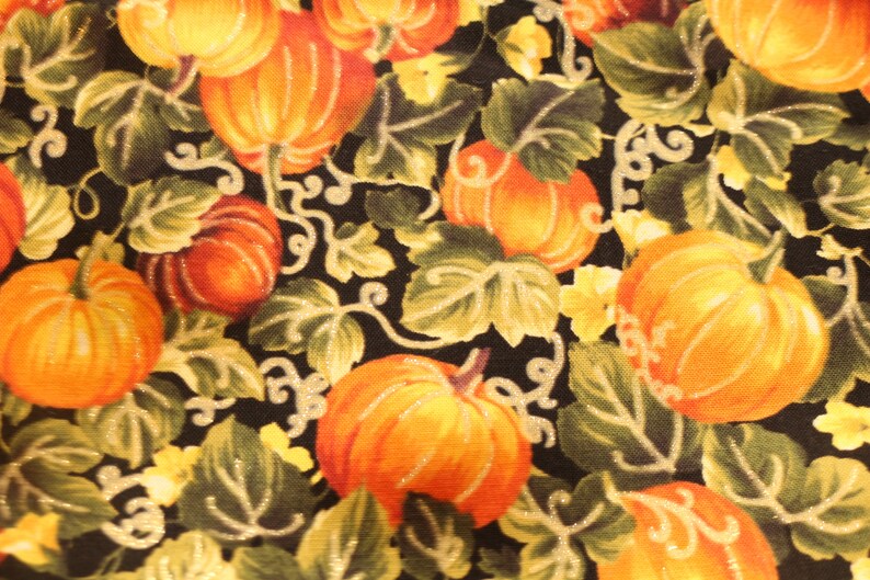 May include: A black fabric with a repeating pattern of orange and yellow pumpkins with green leaves. The pumpkins are various sizes and shapes.
