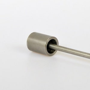 Op de afbeelding: Een zilveren metalen staaf met een cilindrische eindkap. De staaf is ongeveer 25 cm lang.